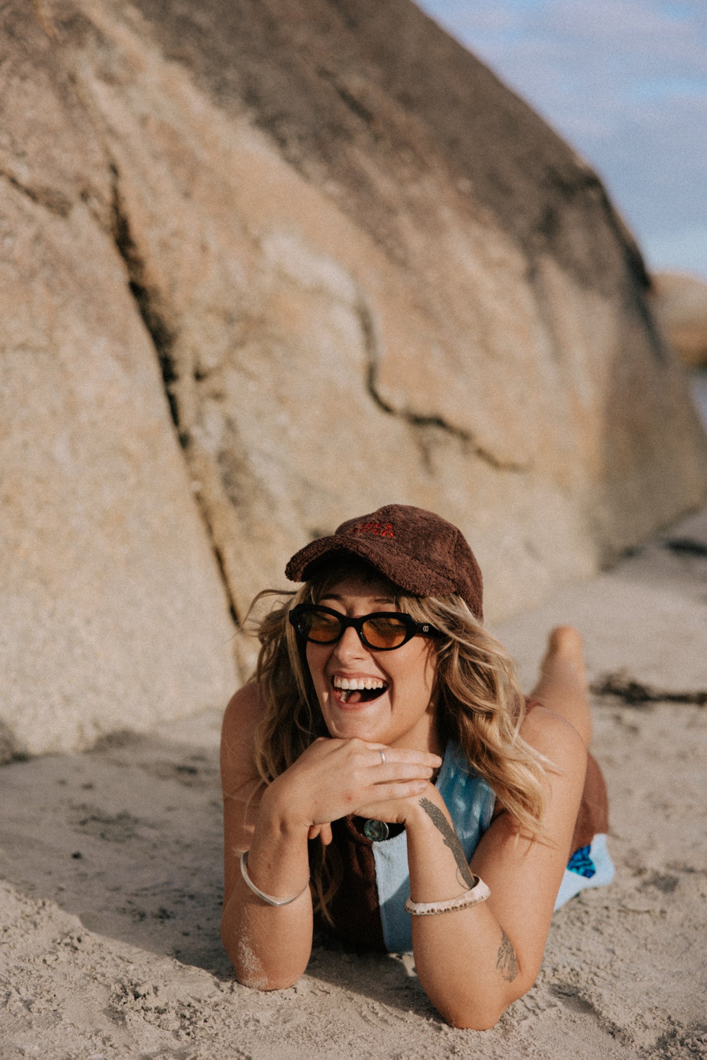 Woman lying on the sand with a large rock and clear sky in the background