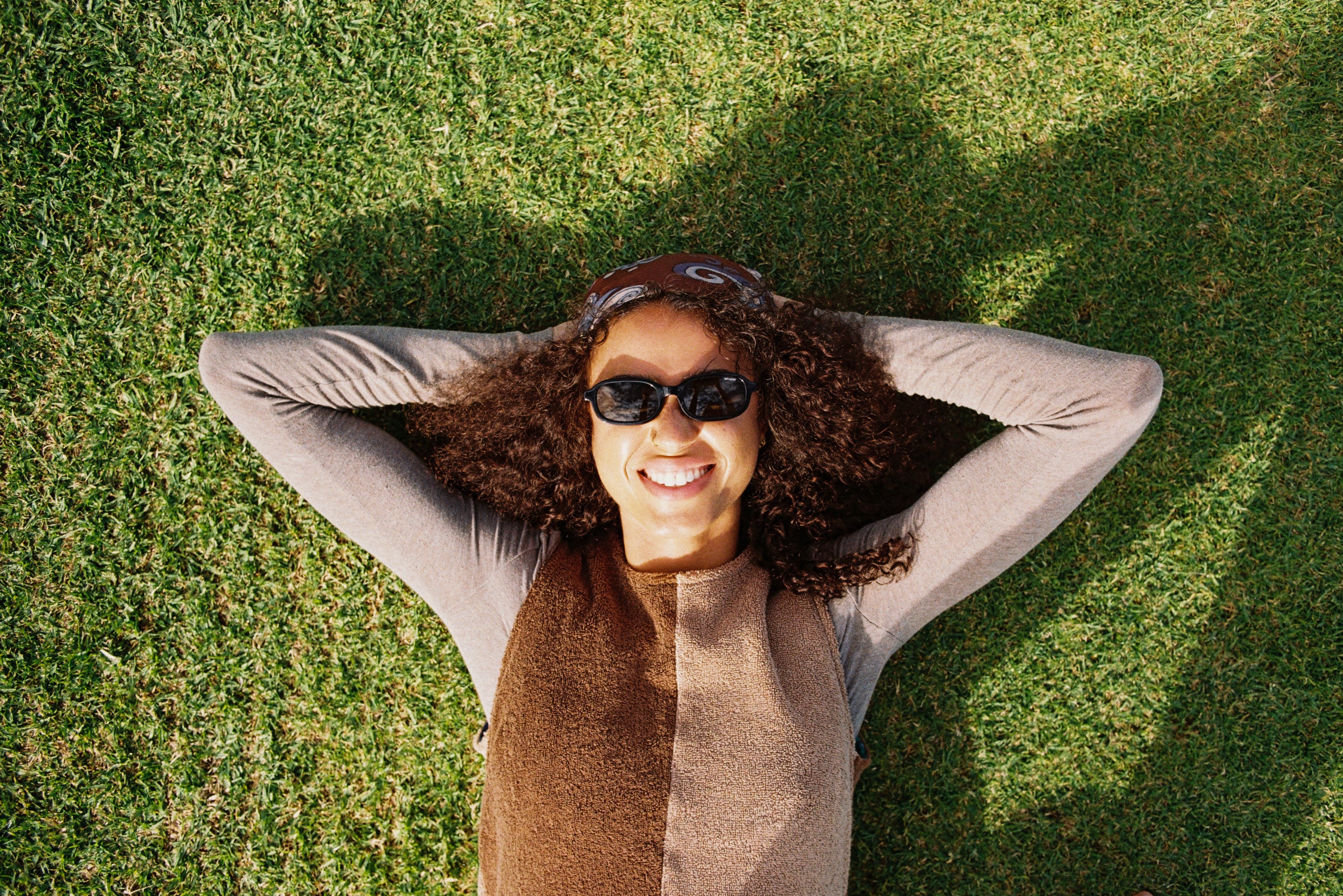 Person lying on grass with arms behind head, wearing Della Dress, sunglasses and a hat
