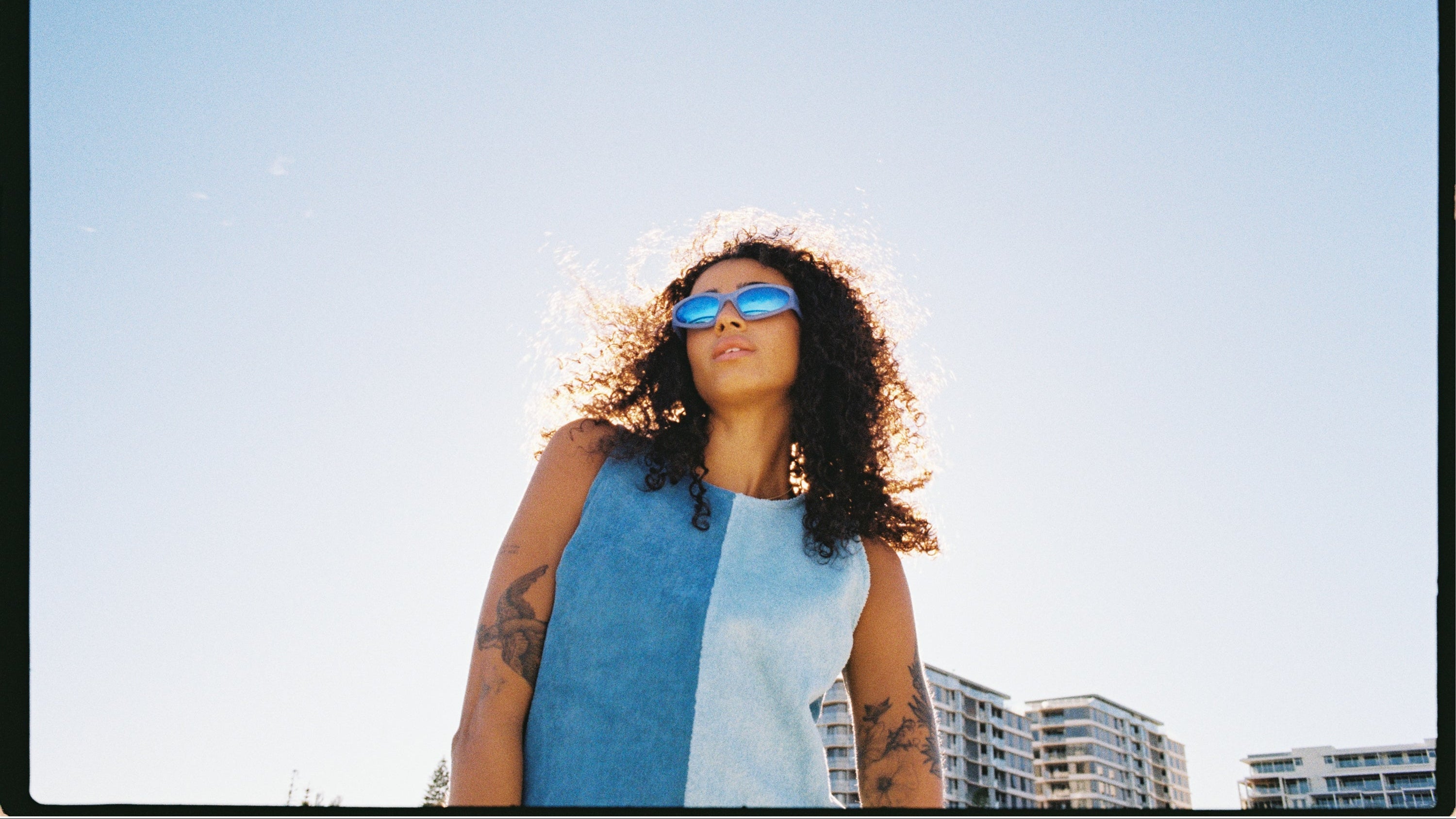 Woman wearing sunglasses and She's Apples Della Dress with a clear blue sky and buildings in the background